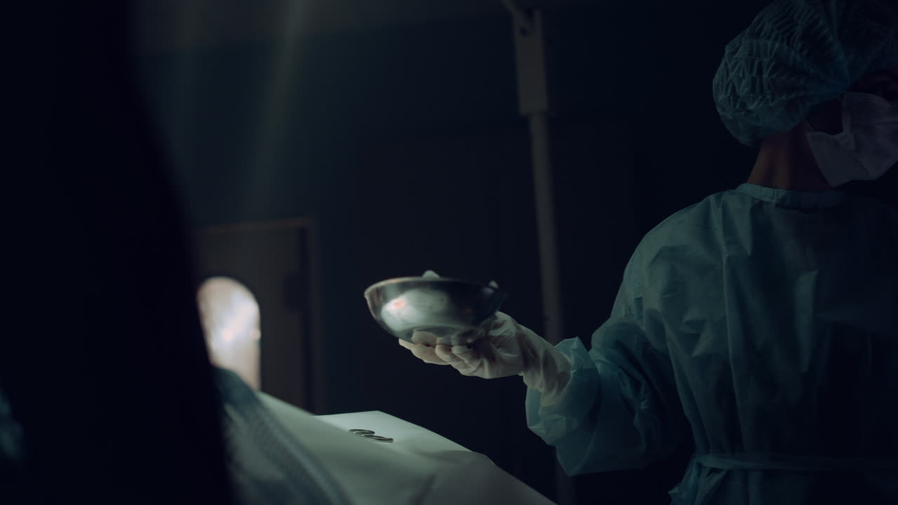 Nurse handing instruments surgeon holding sterile tools in dark emergency room.