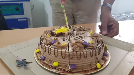 cutting of a round shaped chocolate birthday cake into slices with a knife.