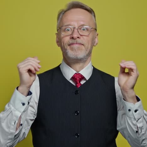 funny grey-haired man putting on glasses. senior man in elegant clothing with eyeglasses making amusing eyes on yellow background. slow motion.