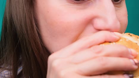 close up of a female biting a burger on a green screen. the concept of unhealthy nutrition and diet