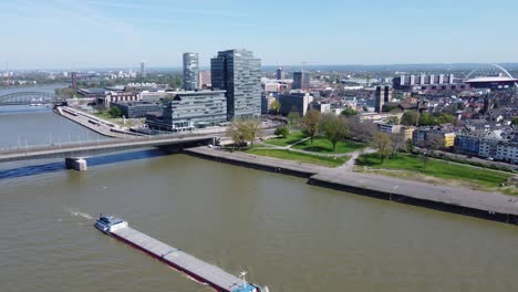 aerial cityscape of industrial ship on urban river with glass corporate buildings in background, cologne