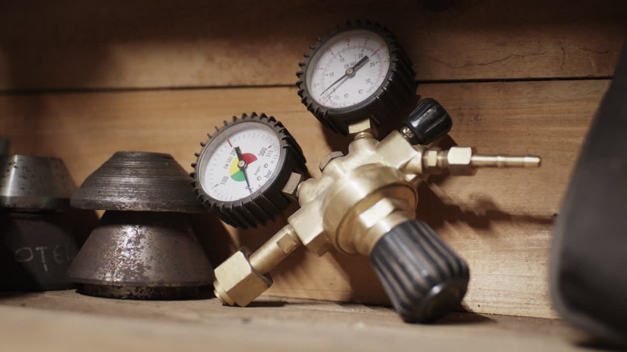 Macro shot of a heavy brass gas cylinder pressure regulator with dual analog gauges resting on a wooden workshop shelf