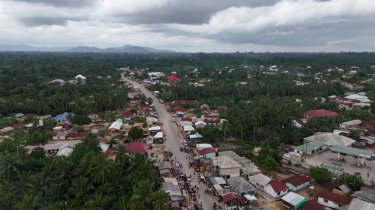 Panorama drone sudut tinggi pemukiman pedesaan Fumso, Ghana. Menampilkan rumah-rumah tradisional yang dikelilingi pohon kelapa yang rimbun dan hutan tropis di bawah langit Afrika Barat yang berawan.
