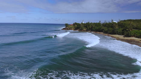 rincon puerto rico surfers riding waves near a lighthouse with a green forrest behind them during a clear day with blue sky