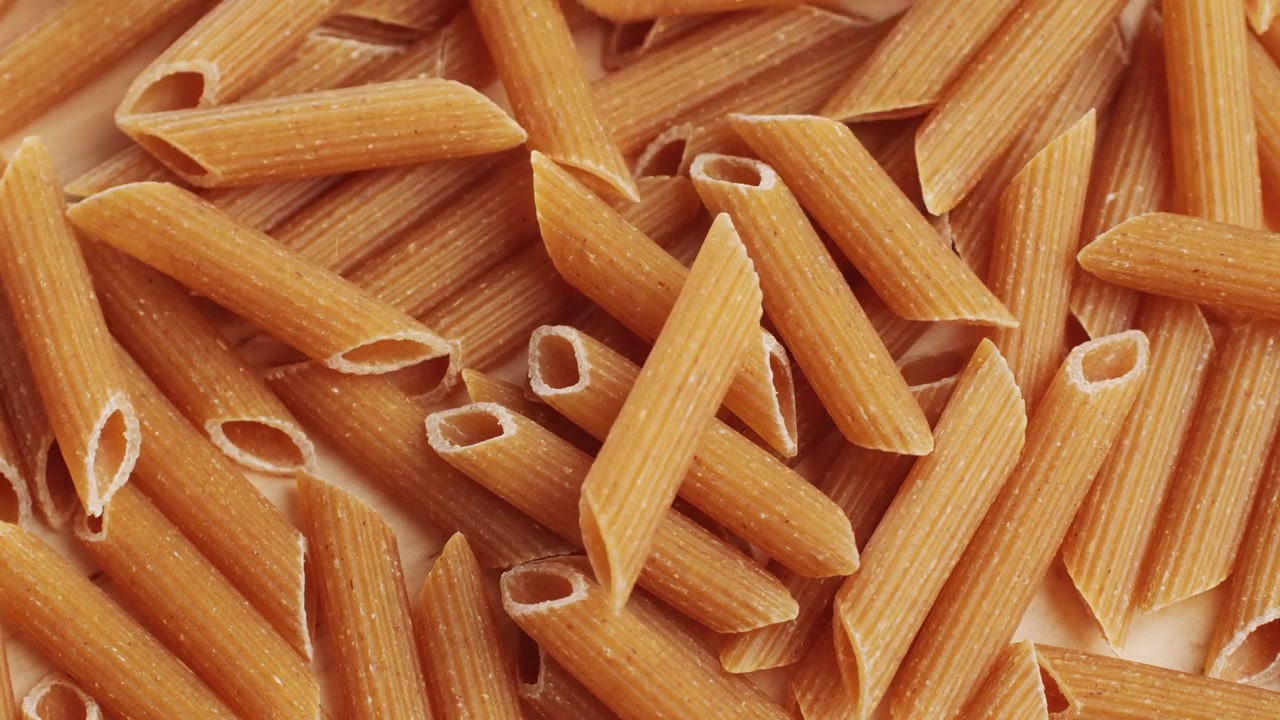 Bio-Vollkornnudeln, Makkaroni aus Hartweizengrieß, ungekochte Penne Rigate in einer Holzschale. Hochwertiges 4K-Filmmaterial