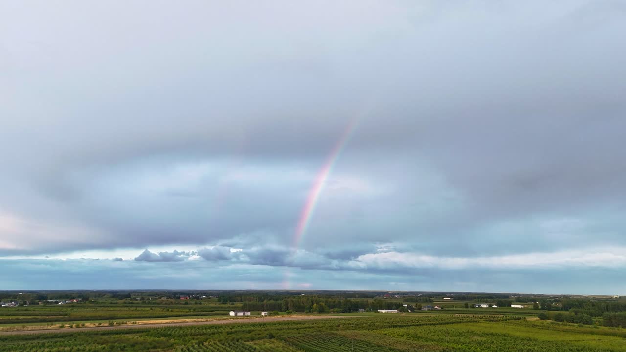 Timelapse of rainbow forming over green field with dramatic rain clouds. Fast-moving sky and vibrant landscape. Ideal for weather, nature, and cinematic travel visuals