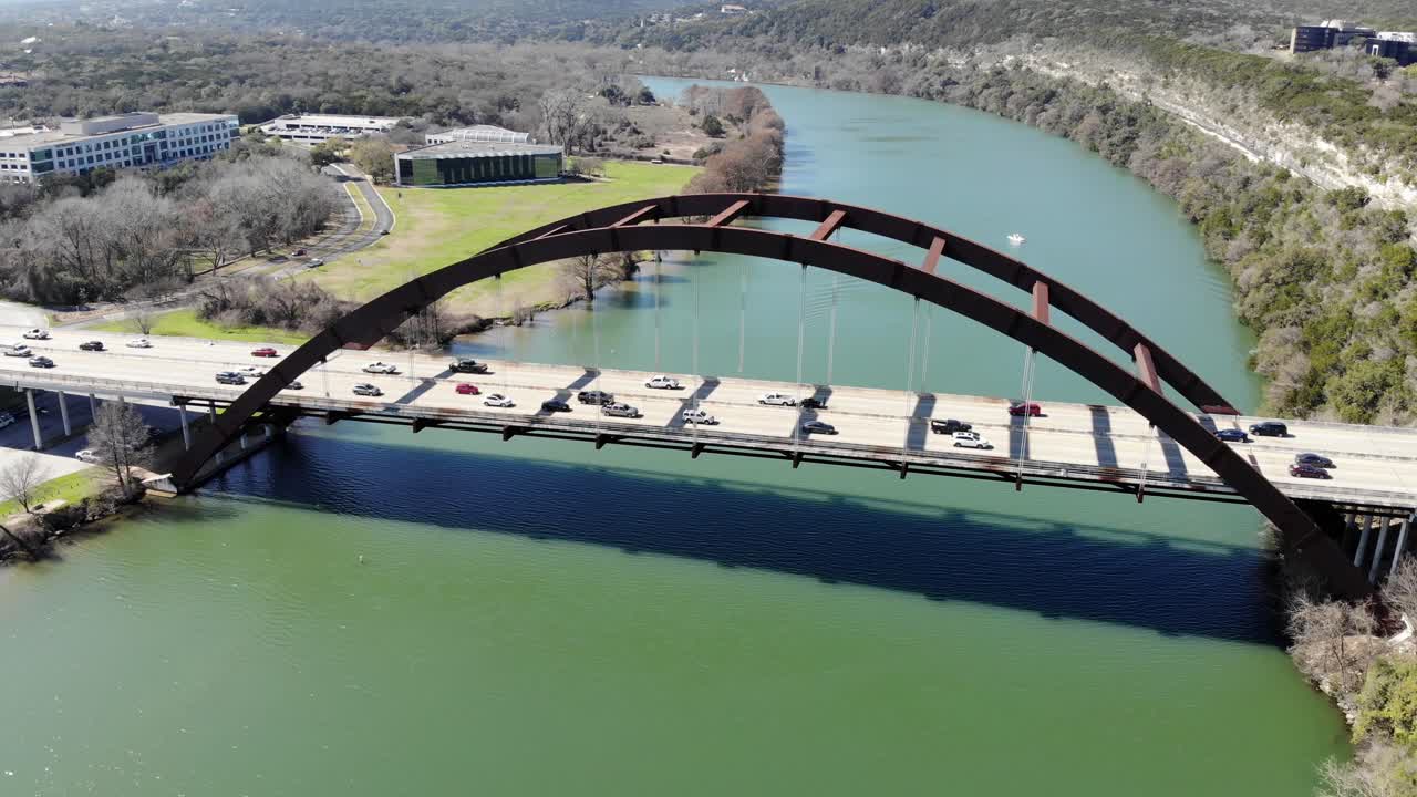 Aerial Austin Pennybacker Bridge - riding above the bridge while traffic is backed up onto the deck, revealing a boat on the other side; moving backwards for a short segment at the end.