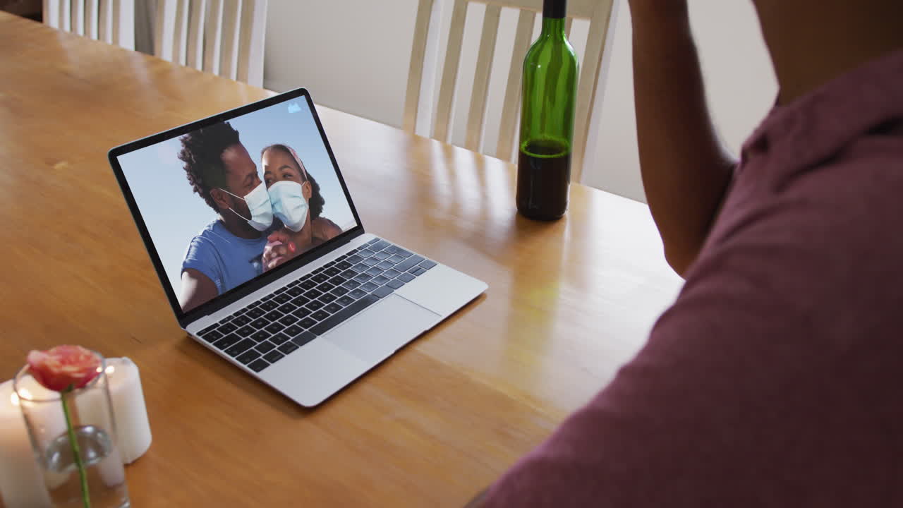 Mid section of african american man drinking wine while having a video call on laptop at home