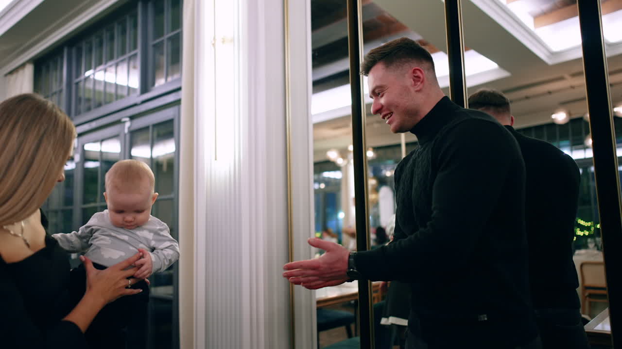 Caucasian woman with child in hands stands in front of the mirrors. Father stretches hands to his son and takes him lifting up. Low angle view.