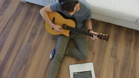 overhead view of asian boy wearing headphones playing guitar looking at the laptop at home