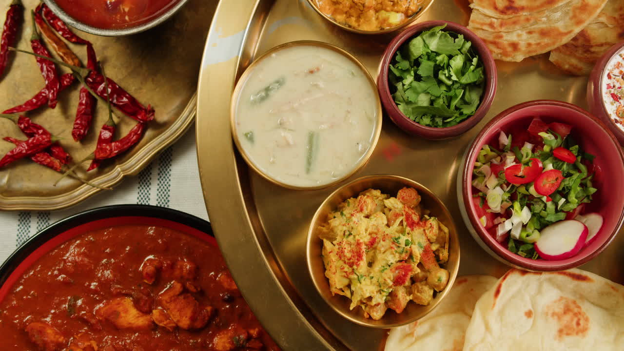 Assorted indian sri-lanka food set on wooden background. Dishes and appetisers of indeed cuisine, rice, lentils, paneer, samosa, spices, masala. Bowls and plates with indian food top view chicken. High quality 4k footage