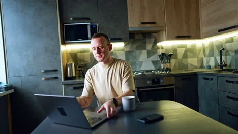 mid-aged caucasian man sits down at the table in the kitchen. man working remote takes a laptop and starts work.