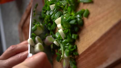 vertical shot of spring onions cutting on wooden chopping board