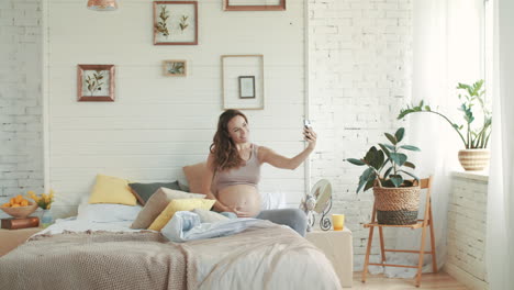 Smiling-pregnant-woman-taking-selfie-photo.-Expectant-mother-sitting-in-bed.