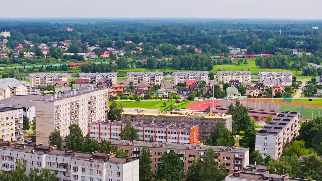 Dron szybuje nad domami w Salaspils, podczas gdy pociąg towarowy przejeżdża przez zielone pola
