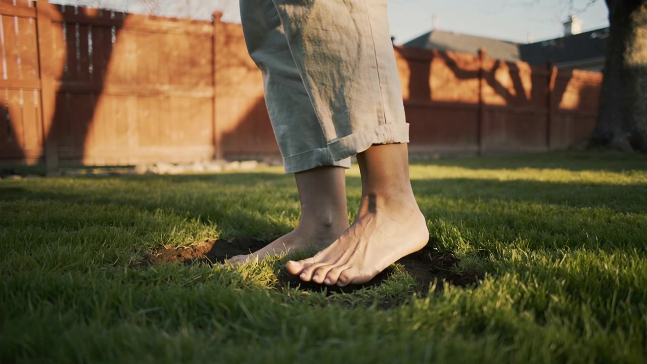 Shifting weight, adult wearing cuffed pants with bare feet lifting then settling in backyard dents
