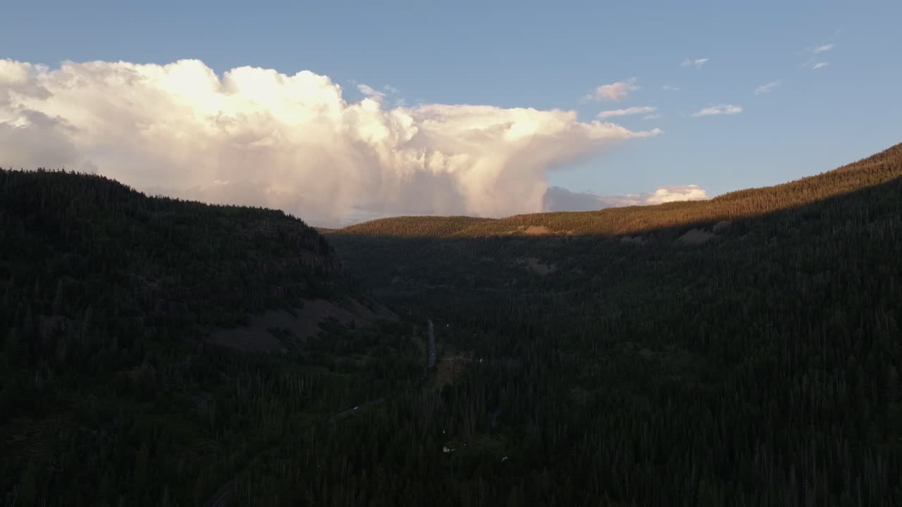 Drone wide shot of the Uinta-Wasatch-Cache National Forest in Utah during a summer sunset, pine trees, Provo River, and Bald Mountain and rain clouds rising above the valley
