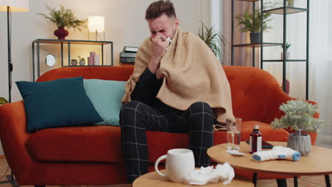 sick ill guy suffering from cold or allergy lying on home sofa sneezes wipes snot into napkin