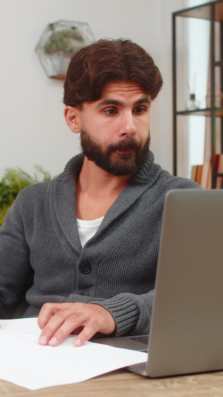 Indian man cross checks numbers on laptop versus paper reports focused data review serious look calm