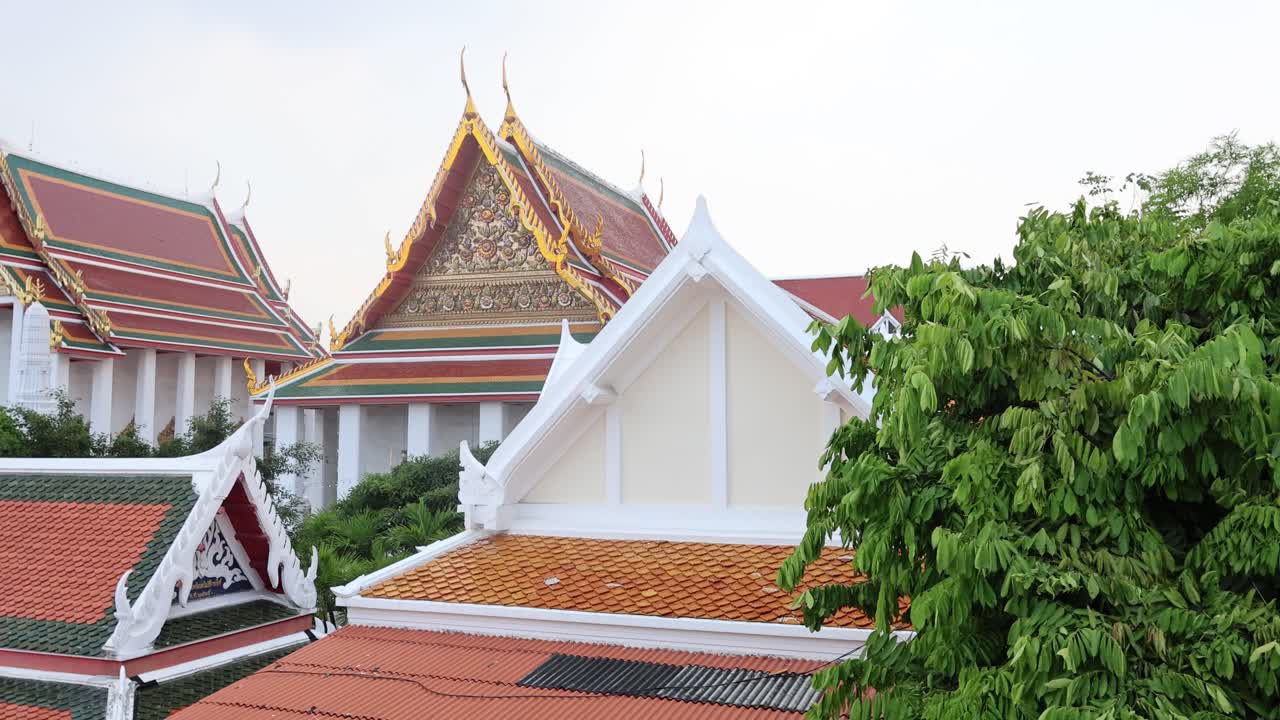 A tranquil scene of Wat Prayurawongsawat's ornate rooftops and lush greenery under soft daylight in Bangkok, Thailand