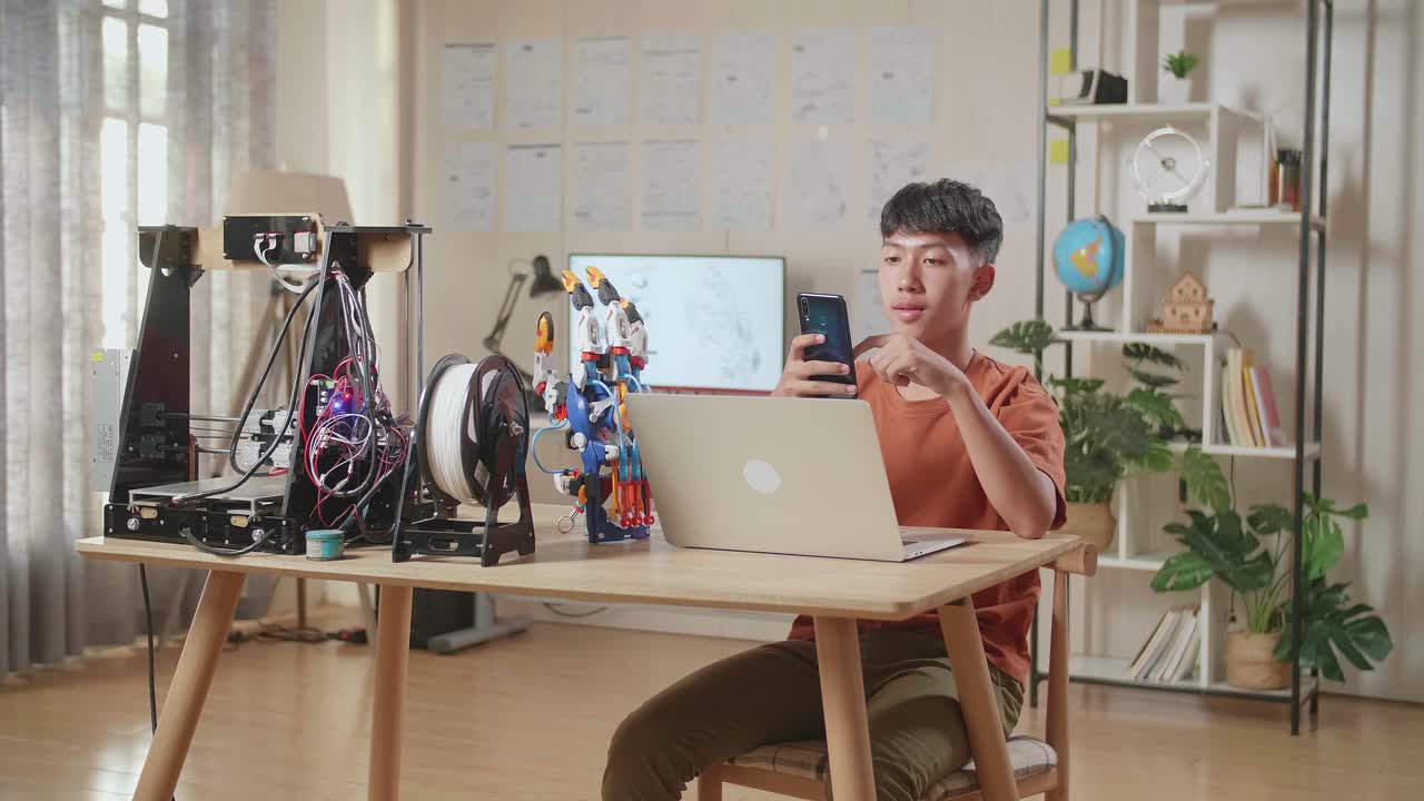 집에 있는 노트북에서 사이보그 손으로 작업하는 동안 스마트폰을 사용하는 아시아 소년