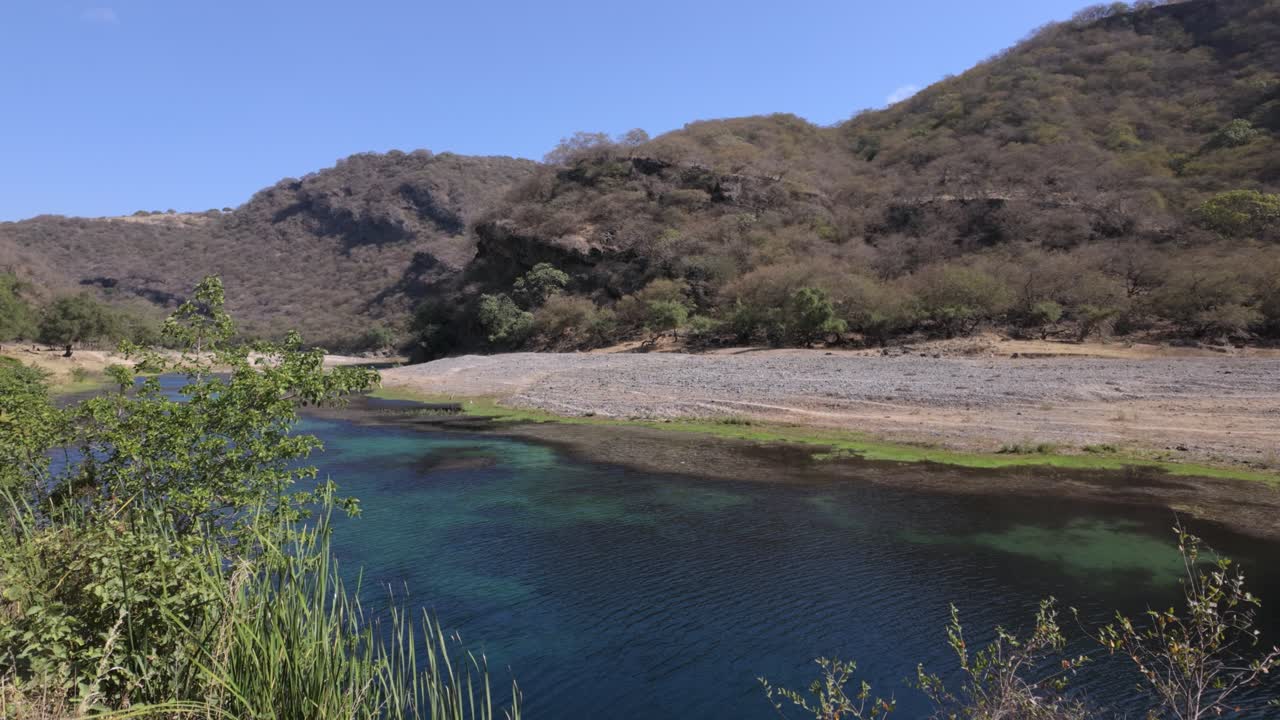 Wadi Darbat oasis near Salalah, Oman with a view of the mountain landscape and turquois freshwater river on a breezy day