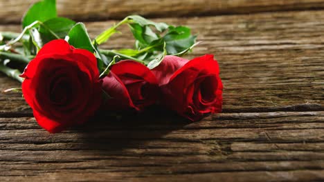 tres rosas rojas en una superficie de madera 4k