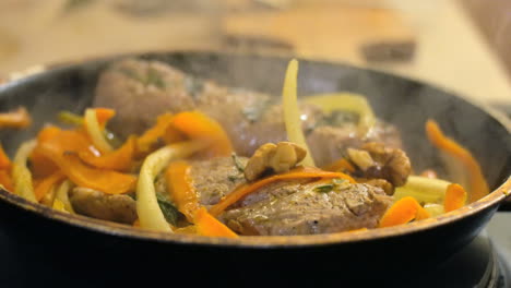 primer plano de carne frita y verduras en una sartén mientras el vapor se eleva desde la carne