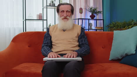 Senior grandfather man sitting on sofa closing laptop pc after finishing work in living room at home