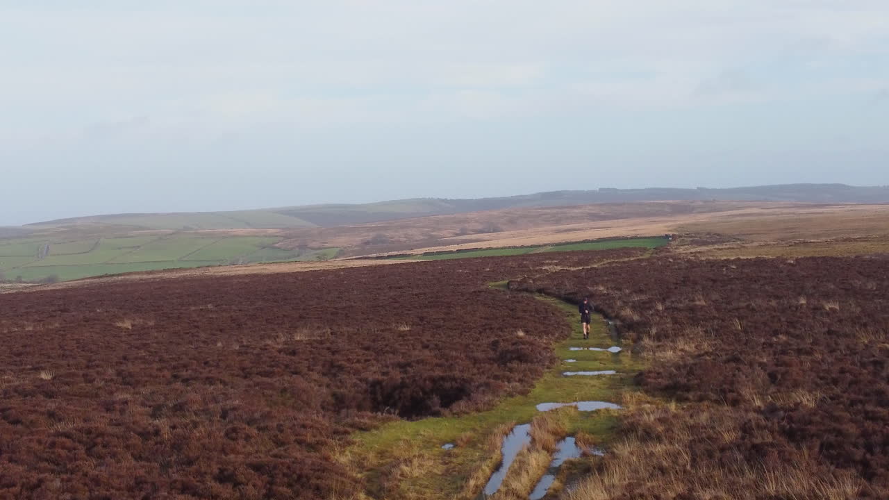 corredor masculino atleta trotar sobre terreno de campo de páramos en régimen de entrenamiento de invierno mantenerse en forma estilo de vida saludable - drone aéreo uk 4k