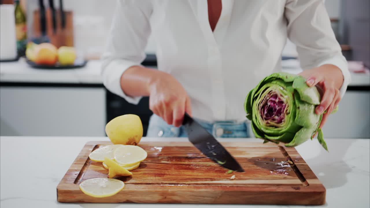 Woman cutting up an artichoke on a wooden cutting board with lemons on it
