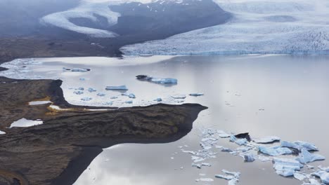 shrinking glacier of fjallsárlón with large water lagoon and icebergs, aerial