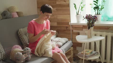 young woman knitting wool sweater on couch in cozy room. woman knitting wool