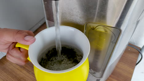 hand of a girl adding hot water from dispenser in a cup with dry green tea leaves