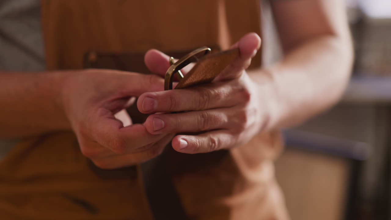 Craftsman puts brass buckle onto leather belt in workshop