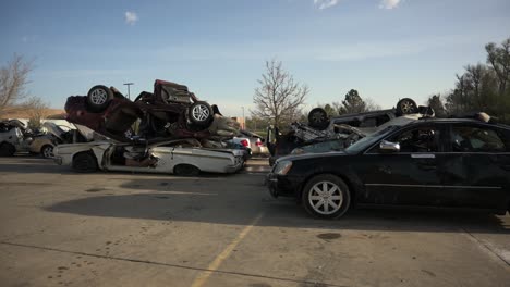 demolished and wrecked vehicles stacked on top of each other in a parking lot, pan