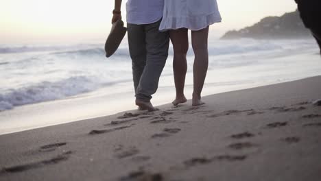 Slow-motion-handheld-shot-of-a-couple-in-love-during-a-romantic-walk-on-the-beach-with-their-dogs-leaving-footprints-in-the-sand-in-calm-waves