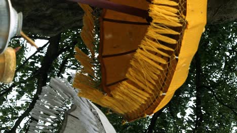 primer plano vertical de paraguas balinesas tradicionales amarillas y blancas con franjas ondulantes en el viento con vistas a las ofrendas y una estatua de bebé en el fondo en bali, indonesia
