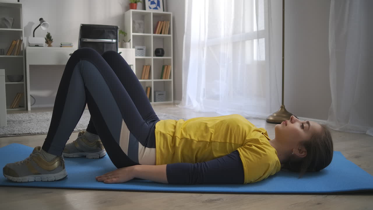 entrenamiento matutino en casa niña adolescente está entrenando sola en la sala de estar acostada en el suelo y levantando las caderas tensando los músculos abdominales y de la espalda estilo de vida saludable