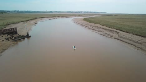 Mann,-Der-Auf-Einem-Sich-Schlängelnden-Fluss-Kajak-Fährt,-Drohne-Folgt-Und-Schwenkt-Nach-Oben,-Um-Eine-Wunderschöne-Landschaft-Im-Hintergrund-Zu-Enthüllen