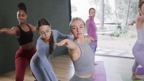 instructora femenina diversa ayudando a las mujeres a practicar la pose del guerrero 2 en la clase de yoga