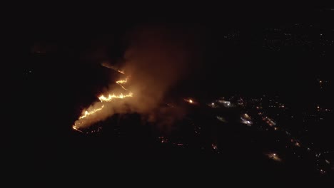 fuego de cepillo en la ladera de la montaña con luces de la ciudad en fondo oscuro