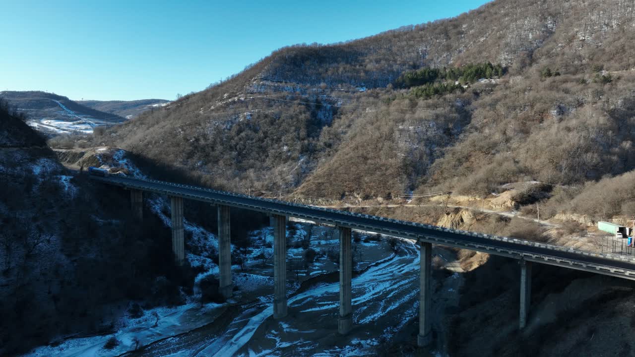 A modern highway elevated on tall pillars traverses a rugged mountain pass, blending engineering marvels with the natural beauty of the snowy landscape