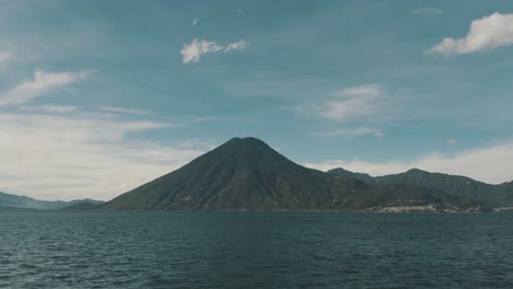 drone aerial view flying close by the blue water of lake atitlan, guatemala and a big volcano in the background