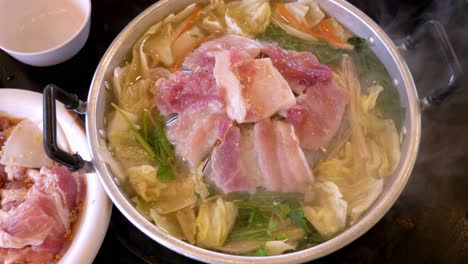 clear vegetable soup topped with pork strip meat simmering in an open pan steaming