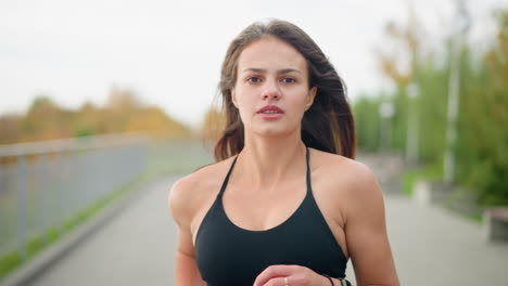 close-up of woman in black singlet jogging, with blurred background of park featuring benches and trees, capturing active lifestyle, fitness, and outdoor exercise