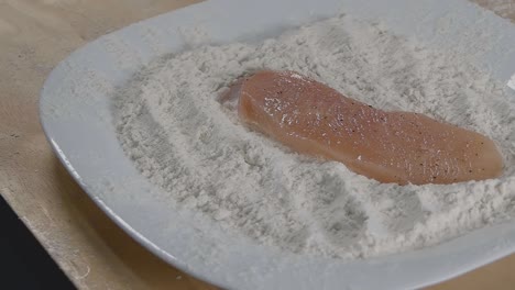 slow motion slider shot of a chicken breast portion landing in flour