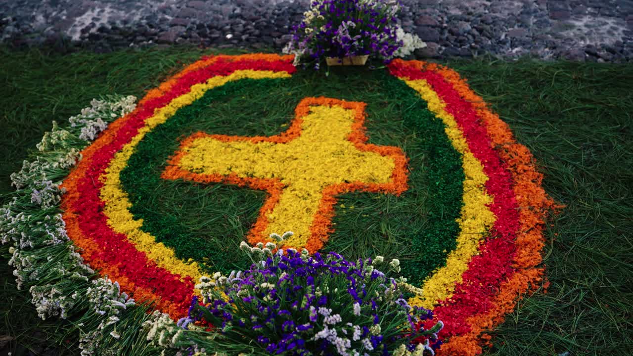 Vibrant sawdust and flower alfombra forming a cross design on a cobblestone street during Semana Santa in Antigua Guatemala