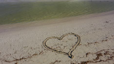 La-Cámara-Se-Inclina-Hacia-Abajo-Desde-El-Horizonte-Mostrando-El-Mar-Con-&quot;Te-Amo&quot;-Escrito-En-La-Arena-De-Una-Playa.