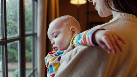 mother holding baby by a rainy window